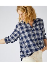 Camicia a quadri navy e bianca con design a bottoni, tasche sul petto, maniche arrotolate e vestibilità rilassata. Tessuto morbido con una sottile texture.