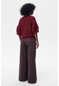 Bordowy sweter z krótkimi, bufiastymi rękawami, w połączeniu z szerokimi, ciemnobrązowymi spodniami. Miękka faktura, minimalistyczny design.