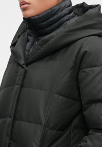 Sort pufferjakke med hætte, der har en quiltet tekstur, en lynlåsfront og en høj krave for ekstra varme og beskyttelse.