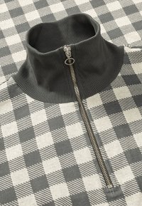 Pull à fermeture éclair gris et crème avec un col montant et un motif à carreaux. Présente une texture côtelée et des détails en zip argenté.