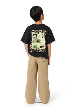 Enfant de dos portant un tee-shirt graphique noir avec des motifs artistiques verts et beiges et un pantalon large couleur beige avec un texte sur la poche arrière.
