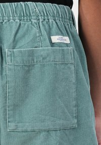 Corduroy shorts in teal with an elastic waistband. Features a back patch pocket and a visible brand label with blue text.