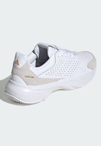 Baskets blanches de sport avec des accents en daim, tige perforée et semelle texturée. Présente un logo de marque doré et un design rembourré.