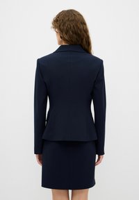 Granatowa, dopasowana marynarka o usztywnionych ramionach i fasonie peplum, zestawiona z dopasowaną spódnicą ołówkową, wykonana z gładkiego materiału.