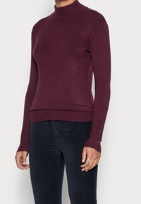 Bordowy sweter z golfem i długimi rękawami, ściągacze z guziczkami oraz dopasowany fason. Miękka, dzianinowa faktura.