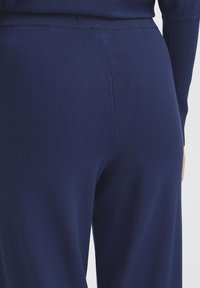 Námořnické modré elastické kalhoty s hladkou texturou, které mají přiléhavý pas a jednoduchý, minimalistický design na zadní straně.