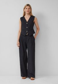 Donker gestreepte op maat gemaakte gilet met een V-hals en gouden knoopsluiting, gecombineerd met brede bijpassende broek. De outfit heeft een soepele textuur.