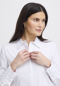 Camicia bianca con colletto classico, taglio slim e maniche lunghe. Il materiale sembra liscio e leggero. Nessun motivo o dettaglio degno di nota.