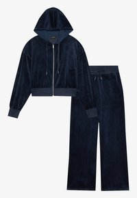 Conjunto de roupa de lazer em veludo azul marinho, composto por uma sweatshirt curta com fecho éclair e capuz, e calças de perna larga, ambas com punhos em bainha e cintura com cordão.