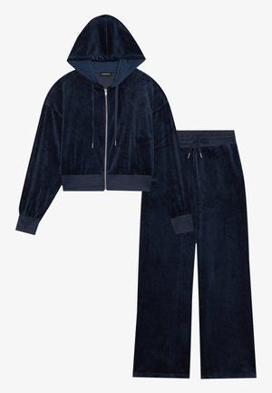 Navy blå velour loungewear-sett med en kort zip-up hettejakke med hette og vide bukser, begge med ribbestrikkede mansjetter og snor i livet.