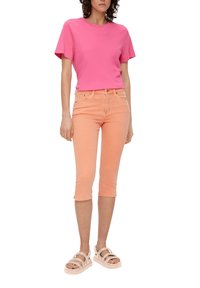 Helles pinkes T-Shirt mit kurzen Ärmeln, kombiniert mit helloranfarbenen cropped Jeans. Das Outfit wird durch beige Plateausandalen mit mehreren Riemen ergänzt.
