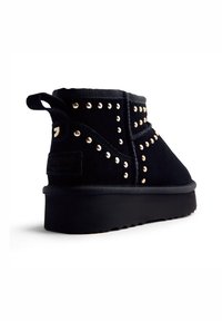 Botas de tobillo de ante negro con tachuelas doradas en los laterales, un tacón reforzado y una suela de goma negra texturada. Pequeña tira en la parte trasera.
