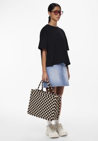 Svart oversize t-shirt, jeanskjol, rutigt axelväska i beige och svart, kombinerat med kraftiga vita sneakers och vita strumpor.