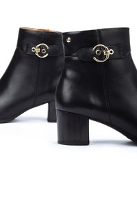 Bottines en cuir noir avec une finition lisse, un talon bloc et un détail de boucle circulaire dorée sur la sangle de cheville.