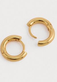 Χρυσά σκουλαρίκια κρίκοι με γυαλιστερή, λεία επιφάνεια. Διαθέτουν κυρτό σχέδιο και κλείσιμο με μεντεσέ, δημιουργώντας μια μινιμαλιστική αισθητική.