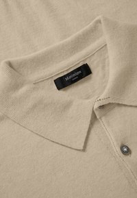 Beige gebreid shirt met een kraag en knoopsluiting, met een zwart label met de tekst "Matinique Europe" genaaid aan de binnenkant van de halslijn.