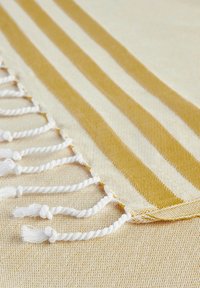 Tessuto di cotone con un motivo a righe gialle e crema. Presenta frange bianche ai bordi, una tessitura morbida e una finitura soffice.