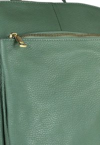 Groene leren tas met textuur, voorzien van een gouden rits trekker op een voorvak, met gedetailleerde stiksels en nerf van het materiaal.