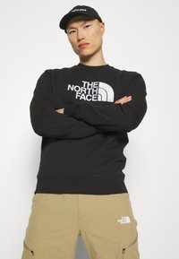 Sudadera negra con un gran logo blanco de "The North Face". Hecha de un material suave, con cuello redondo y puños acanalados.
