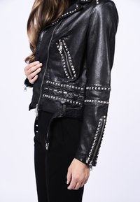 Veste de motard en cuir noir avec des accents en clous argentés, des poches zippées asymétriques et des fermetures éclair sur les manches. Texture lisse et coupe ajustée.