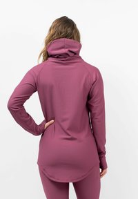 Fitted long-sleeve top in ribbed, magenta fabric with a high collar. Features a curved hem and thumbholes at sleeve cuffs.