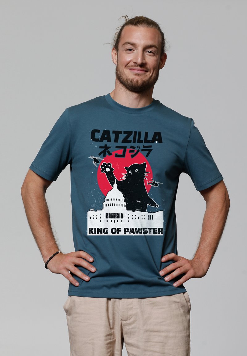 T-shirt en coton teal avec un design graphique représentant un grand chat sur le bâtiment du Capitole, avec le texte "CATZILLA" et "KING OF PAWSTER".