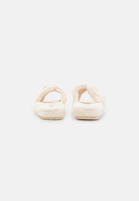 Cream-colored slippers with a soft, plush texture, featuring two crossover straps and a textured sole for grip.
