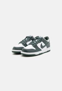 Une paire de baskets basses avec des panneaux blancs et vert foncé, des lacets vert foncé et une semelle assortie sur un fond clair.