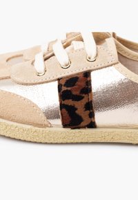 Beżowe trampki z metalicznym złotym i lamparcim wzorem, z sznurowadłami, gładkimi i fakturowanymi powierzchniami oraz teksturowaną gumową podeszwą.