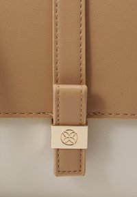 Sac en cuir tan avec fermoir en métal doré orné d'un emblème floral, surface texturée et détails de couture contrastants.