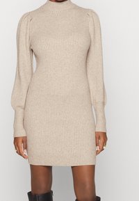 Beige ribbad stickad klänning med hög krage och puffärm, som har en figursydd siluett och strukturerad tyg.