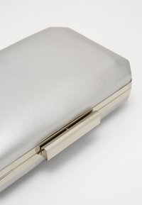 Stříbrná obdélníková kabelka s texturovaným povrchem a metalickým zapínáním. Hladký povrch s zaoblenými hranami a minimalistickým designem.