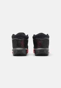 Chaussures de sport noires avec des accents rouges, dotées d'un dessus en maille, d'un col rembourré et d'une semelle en caoutchouc texturé. La vue arrière montre le détail de la marque.