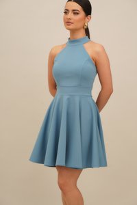 En ermela, halter-neck kjole i lyseblått stoff med tettsittende overdel og flagrende skjørt. Glatt tekstur, knelengde design.