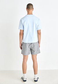 Light blue cotton t-shirt with a crew neck, paired with gray and white striped shorts. Features white sneakers and ribbed socks.