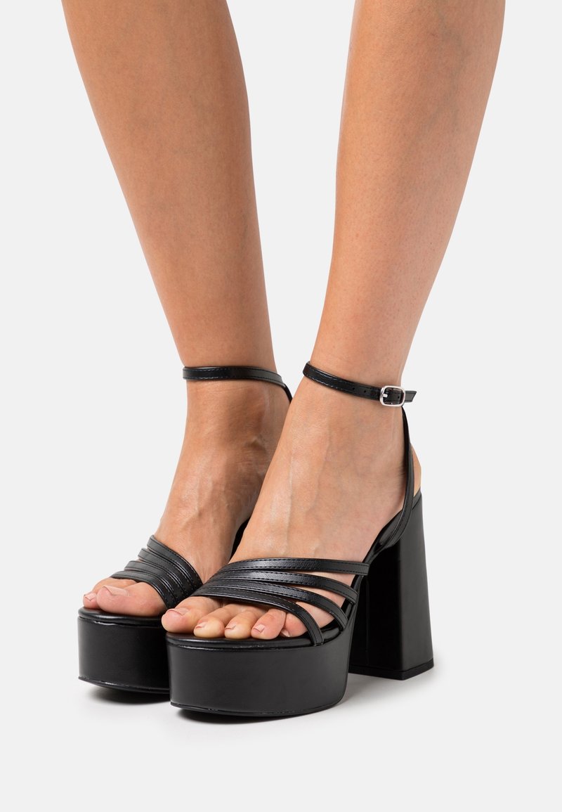 Musta korokepohjainen sandaalit, joissa on useita leveitä hihnoja, nilkkahihna ja paksu korko. Sujuva nahkatextuuri ja tyylikäs muotoilu.