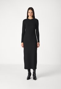 Black ribbed long-sleeve dress with a fitted silhouette, crew neck, and ankle length, paired with black knee-high boots.