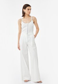 Hvid ribbet tanktop med tynde stropper og knapdetalje. Matchet med løstsiddende hvide bukser, begge i glat stof.