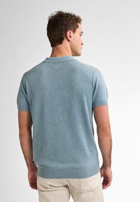 Světle modrá polo tričko s krátkým rukávem vyrobené z měkké pleteniny, s žebrovaným límcem a manžetami, s rovnými okraji a minimálním zdobením.