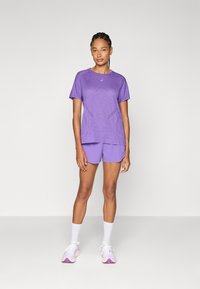 Conjunto atlético morado que incluye una camiseta de manga corta texturizada con patrones geométricos y pantalones cortos a juego, complementado con calcetines y zapatos blancos.