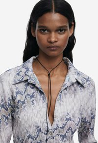 Košeľa na gombíky so štruktúrovaným modro-bielym vzorom hada, so golierom a čiernym šnúrkovým detailom okolo krku.