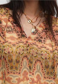 Top leggero multicolore in tessuto, caratterizzato da intricati motivi paisley e floreali in tonalità di arancione, marrone e giallo. Design a V, texture delicata.