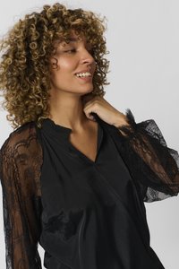 Juoda bliuskutė su permatomomis nėrinių rankovėmis, puoštomis sudėtingais raštais, V formos iškirpte ir lygia, satino kūno dalimi. Tekstūruoti akcentai papildomai pabrėžia eleganciją.