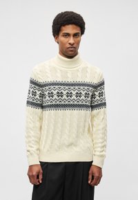 Camisola de gola alta em malha grossa creme com uma faixa estampada em preto e branco atravessando o peito. Punhos e bainha canelados, tecido texturizado.