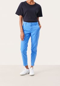 Blå bomullsshorts med en avsmalnande passform, med framfickor och en jämn textur, kombinerat med en svart t-shirt med kort ärm och vita sneakers.