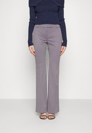 Vrouw draagt hoge taille, brede broek met patroon, gecombineerd met een marineblauw geribd off-shoulder shirt met lange mouwen en zwarte sandalen met open tenen.