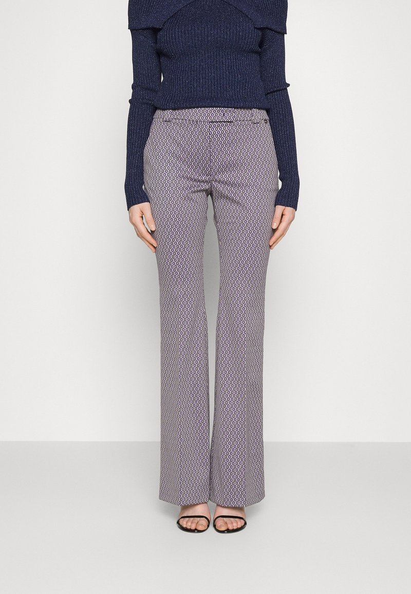 Femme portant un pantalon large à taille haute avec un motif, associé à un haut bleu marine côtelé à manches longues et épaules dénudées, et des sandales noires à bouts ouverts.