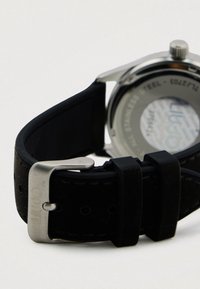 Schwarzes Uhrenarmband aus strukturiertem Material, mit einer silbernen Metallschnalle und einem Edelstahlgehäuse mit einem transparenten Rückenteil.