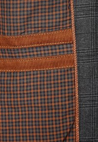 Tissu présentant un motif à carreaux en marron et bleu marine. Comprend des bandes verticales texturées en tissu marron côtelé, bordées de matériau gris foncé.