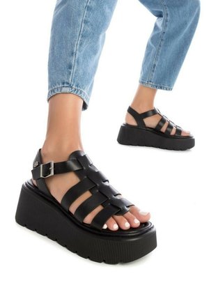 Sandalias negras de cuña con diseño de punta abierta, que cuentan con correas entrelazadas, un cierre de hebilla y una suela de plataforma texturizada.